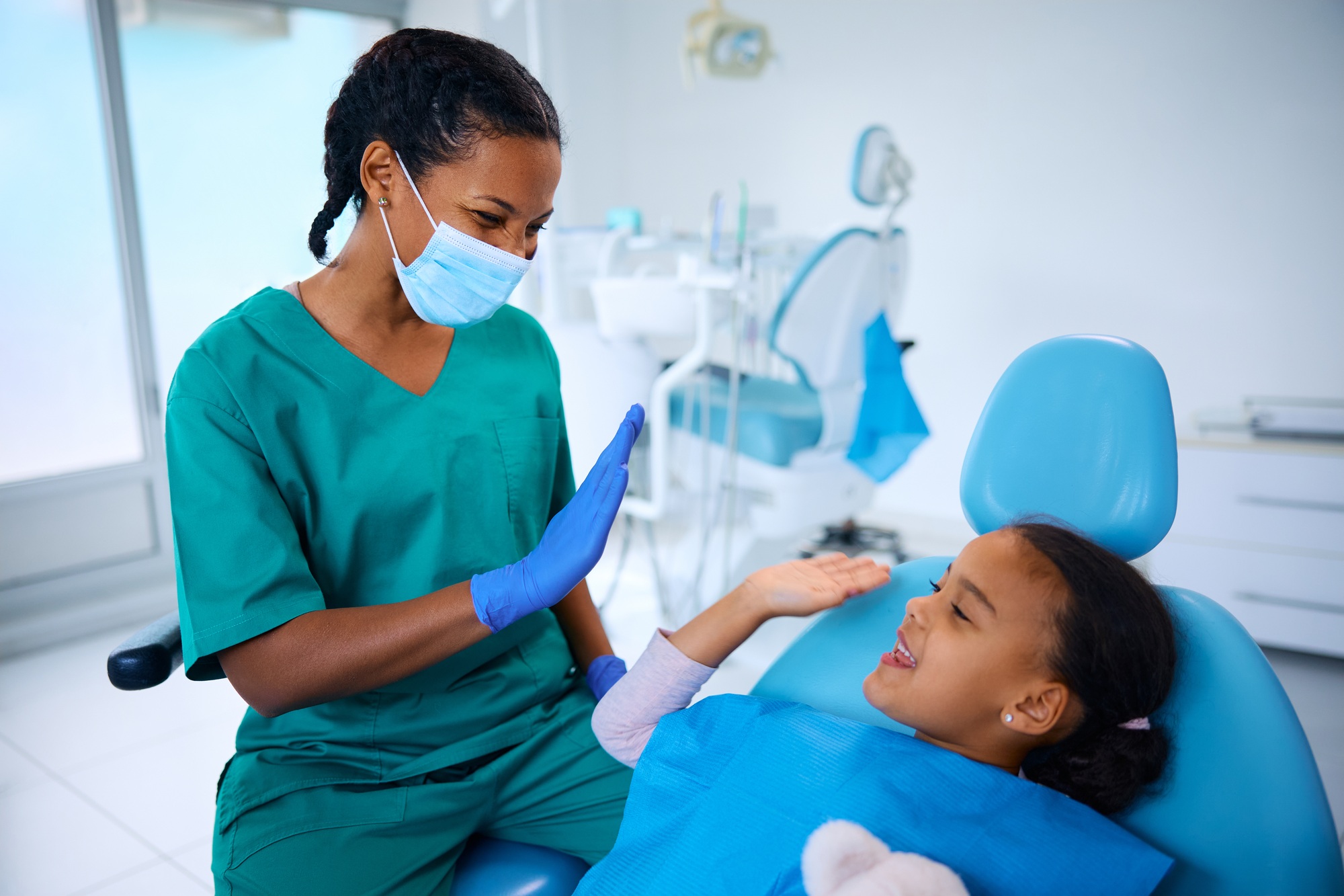 Happy black girl giving high-five to her dentist after teeth check-up.