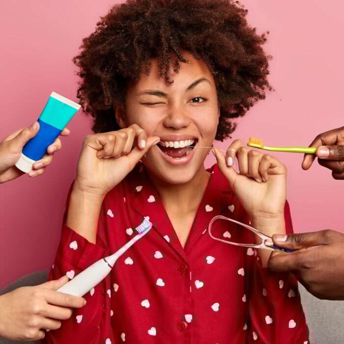 Happy curly young woman brushes teeth with tooth floss, cares about oral hygiene, surrounded with to
