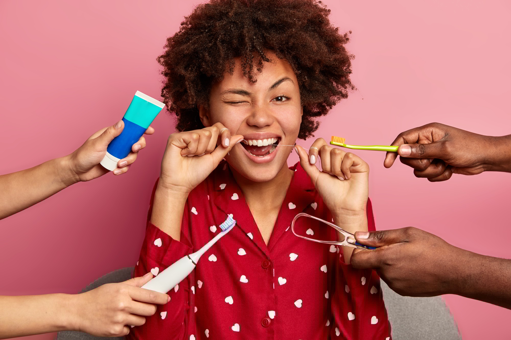 Happy curly young woman brushes teeth with tooth floss, cares about oral hygiene, surrounded with to